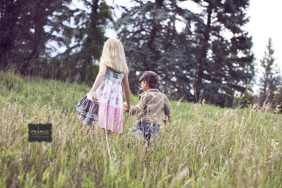 a brother and sister holding hands in a field